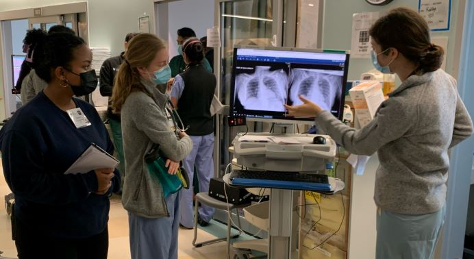 Student to left looks at computer screen with chest xray image with two doctors